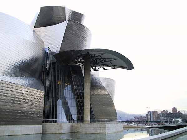 Een gebouw met ronde en puntige vormen in titanium, omgeven door water