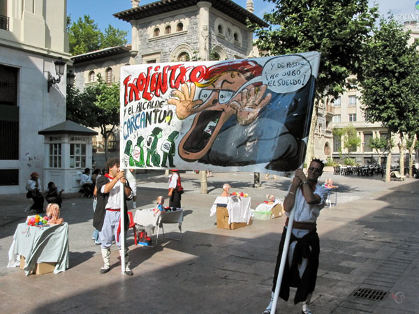 Twee jongens in klederdracht met spandoek met karikatuur en Baskische tekst