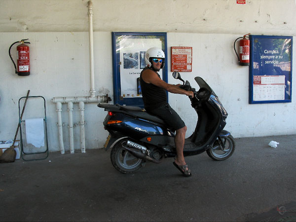 Man in korte broek, met zonnebril, op scootertje