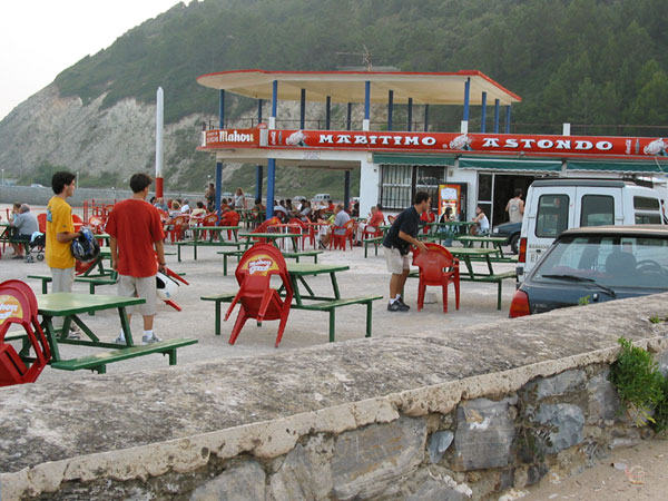 Jongen stapelt rode plastic stoeltjes op, bij strandpaviljoen