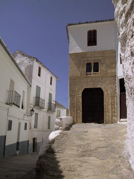 Smal wit huis op verhoging, natuurstenen onderkant met versierde Moorse boog als opening