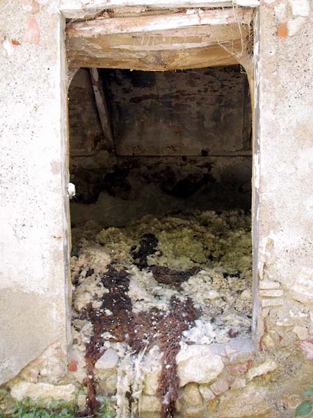 Open deur van vervallen gebouw, resten schapenwol binnen