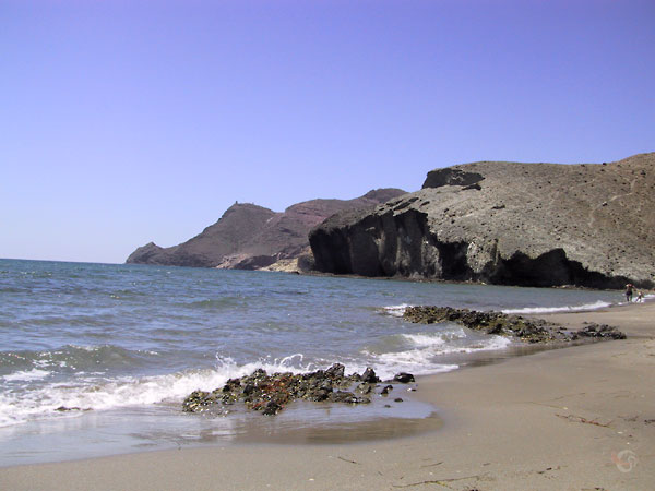 Strandje met blauwe zee en uitstekende zwarte rotsen