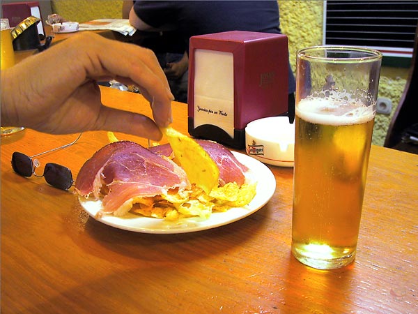 Glas bier, bordje met chips en Serrano ham