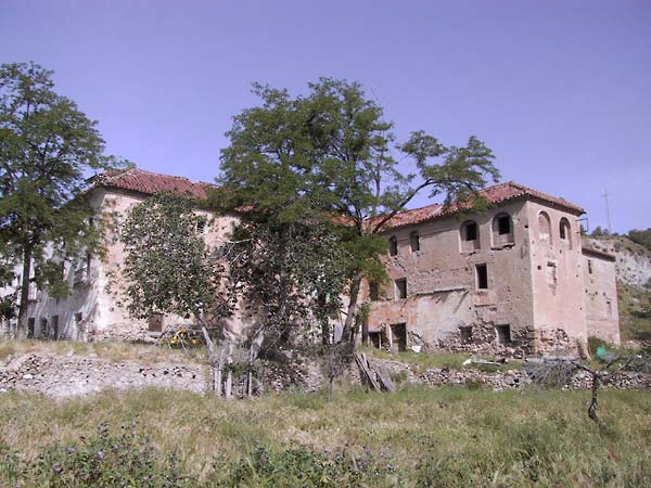 Groot vervallen klooster van baksteen met rood pannendak, op helling met muurtjes en verwaarloosde boomgaard