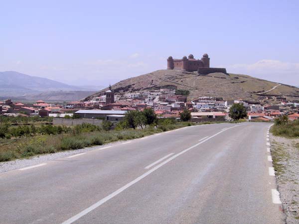 Wit dorpje met heuvel daarachter met kasteel, met vier ronde torens