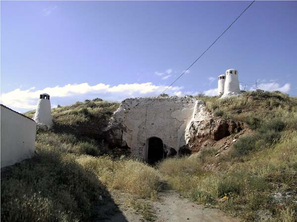 Witte gemetselde ingang naar woning onder heuvel; witte ronde schoorsteentjes er boven
