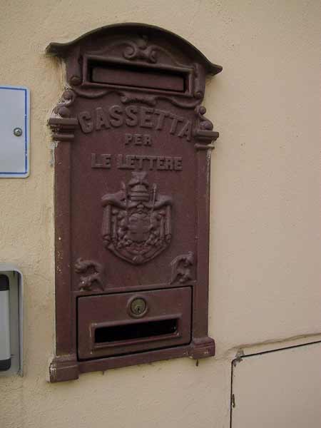 Donkerrode, metalen brievenbus in een muur, met opschrift: Cassetta per le lettere