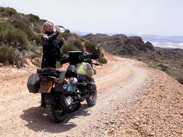 R1100GS on rocky road, Sylvia standing next to it, drinking water