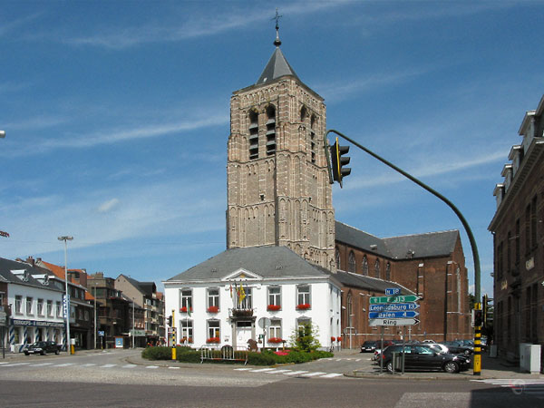 Bakstenen kerk met daarvoor wit huis met geraniums