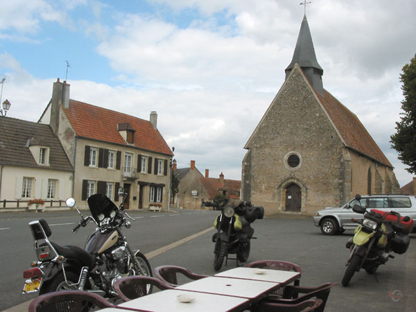 Onze motoren met een motorvriendje bij een terras, kerk op de achtergrond