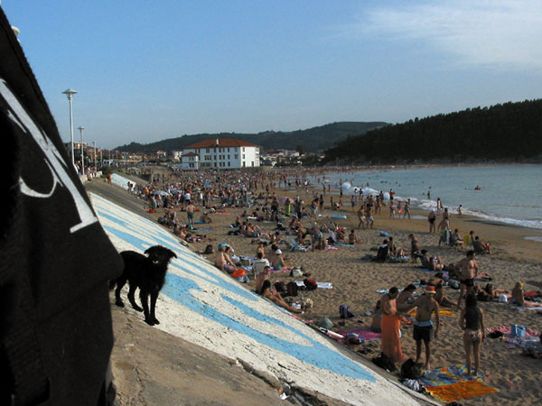 Strand vol mensen, wit huis aan einde baai