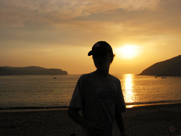 Pieter in silhouet, tegen het licht van de ondergaande zon, met de zee er achter