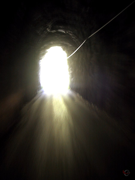 Donker smal tunneltje met verblindend licht aan het eind