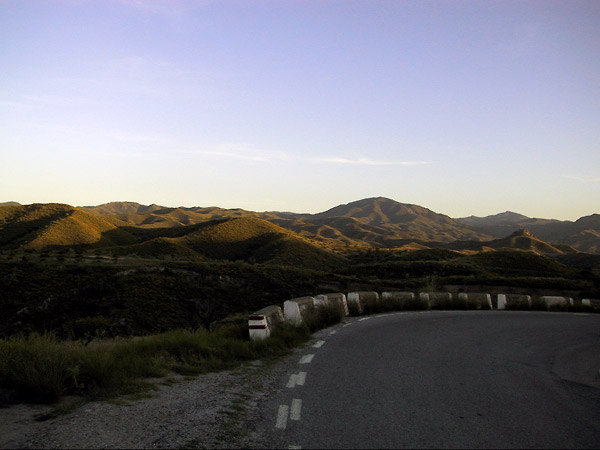 De weg in de schaduw, de toppen van de donkergroene bergen in de zon