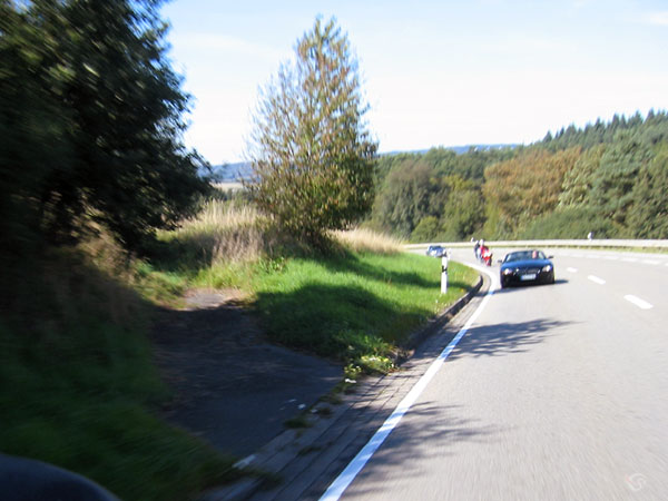 Terugkijkend auto uit de bocht komend, een [paar motorrijders daar achter