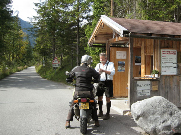 Houten tolhuisje, man in lederhosen, en Sylvia die betaalt