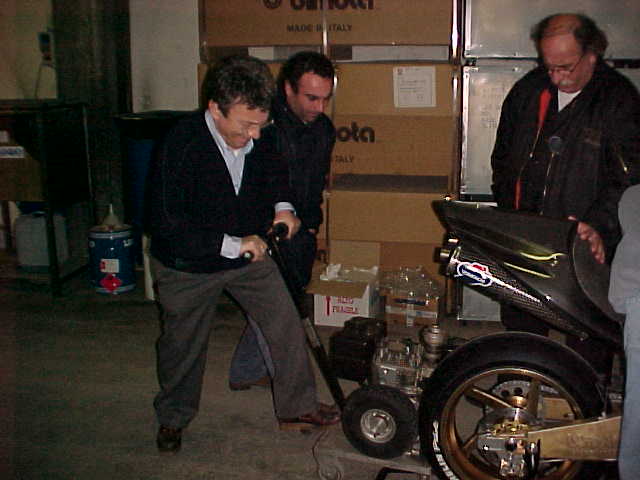 Drie mensen bij de achterkant van een motor, dozen met Bimota er op op de achtergrond