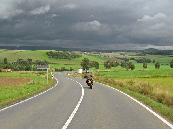 Tricker over weg met lange bocht, donkere wolken