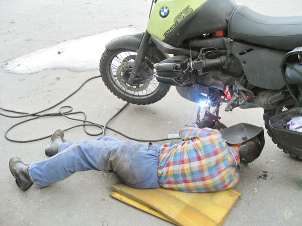 Man ligt op de grond bij de motor met een lasapparaat