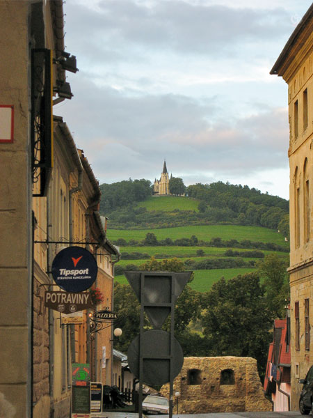 Doorkijkje tussen twee huizen, zicht op groene heuvel met kerk