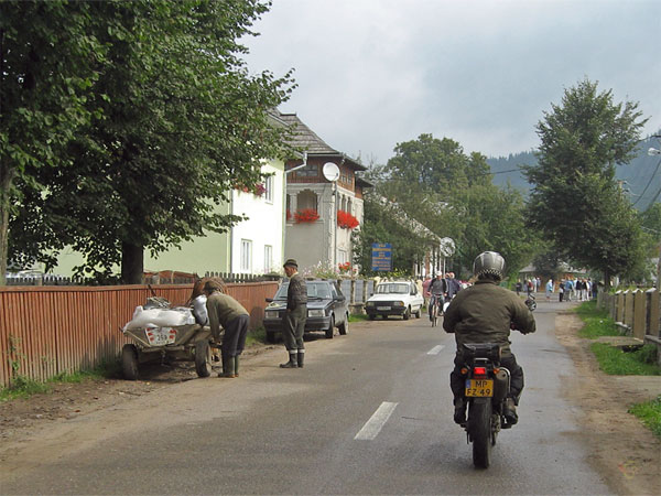 Mensen bij een kar, fietsers, houten hekken rond huizen