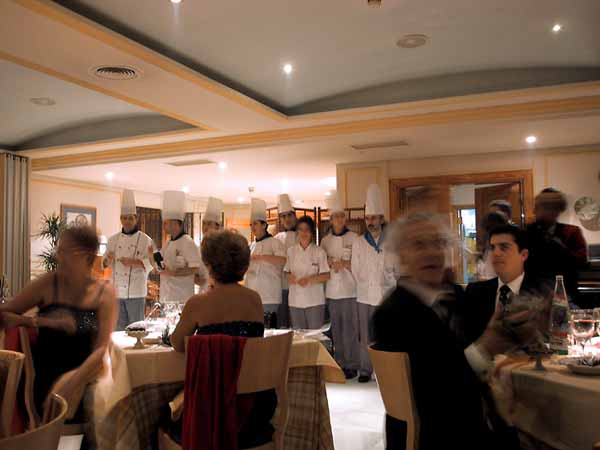 Mensen aan restauranttafeltjes met daar achter de koks op een rij