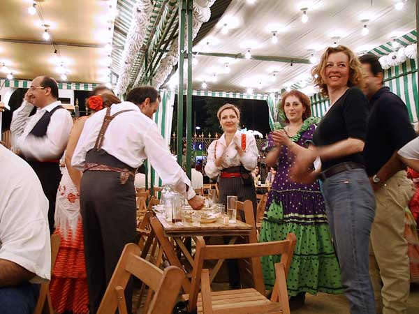 Mensen in Sevillanakleding bij tafel vol eten en drinken