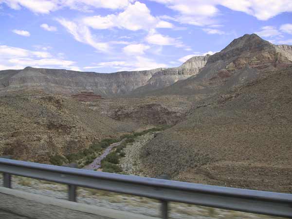 Rechts van de weg een smal stroompje; heuvels met gekleurde banden